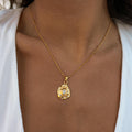 A gold-plated necklace with a molded stone shaped pendant being worn by a person.