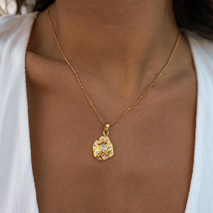 A gold-plated necklace with a molded stone shaped pendant being worn by a person.