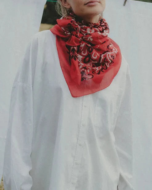 Woman wearing a red embroidered scarf standing in front of white sheets on a clothesline.