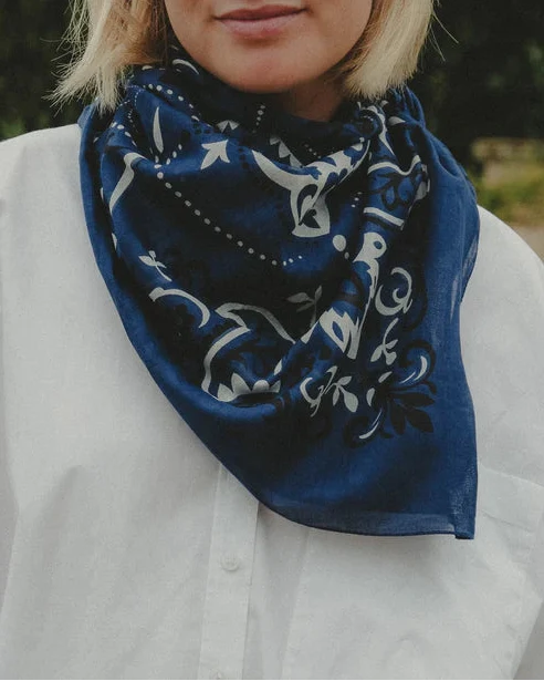 Woman wearing a blue patterned scarf outdoors with greenery in the background