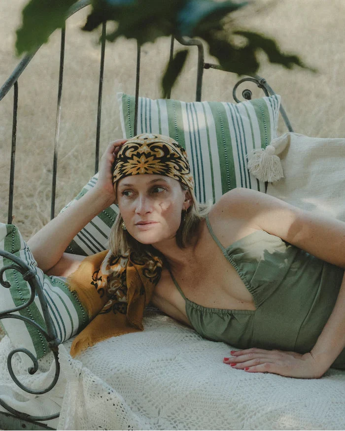 Woman in a green dress and patterned headscarf lying on a sun lounger with green and white striped cushions.