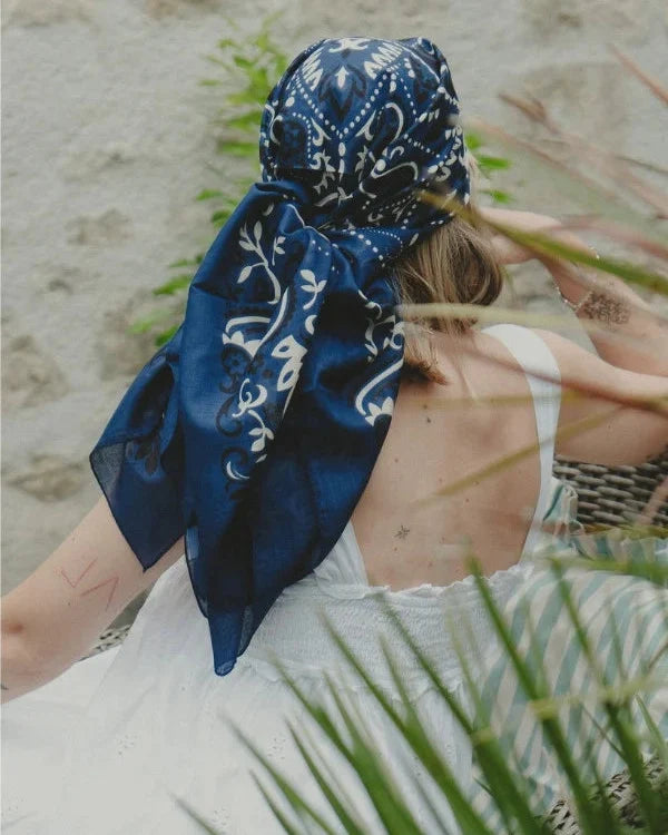 Person wearing a blue bandana with white patterns on a beach.