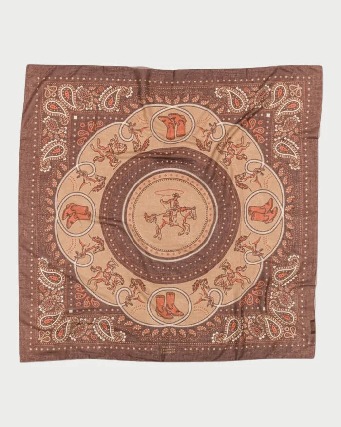 The Maison Lecomte Flament Rodeo Scarf Capuccino is a brown cotton voile scarf featuring a central cowboy on horseback, western motifs like boots, hats, saddles, horseshoes, and a paisley border.