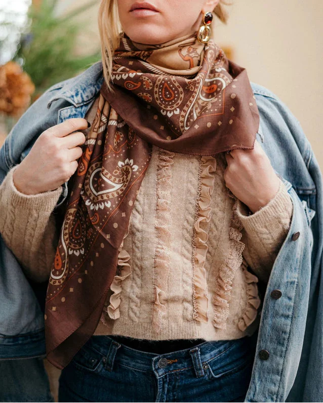 Wearing a Maison Lecomte Flament Rodeo Scarf Capuccino, a cream textured sweater, and a denim jacket over the shoulders, this western-inspired look is styled with long earrings, showcased from shoulders to waist.