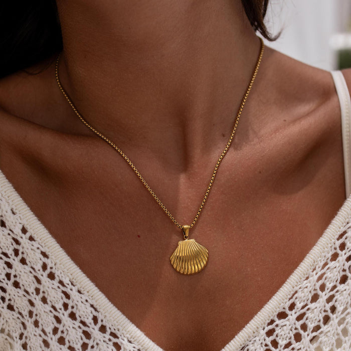 Gold necklace with a shell pendant worn by a person in a white crochet top.