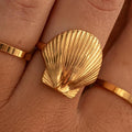 A gold-plated waterproof ring with a shell design worn on a person's finger.