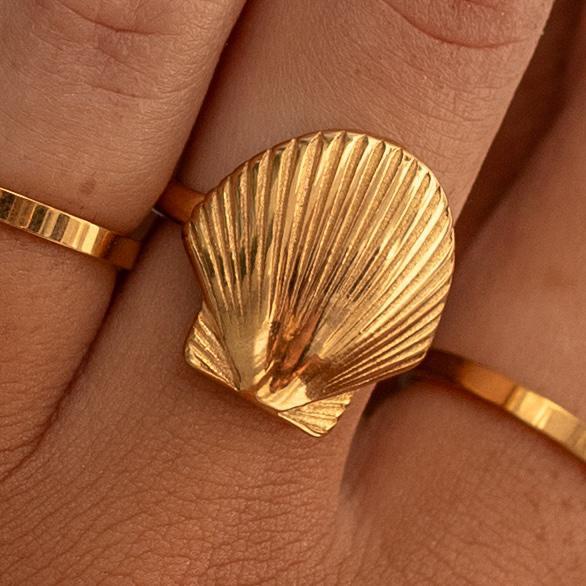 A gold-plated waterproof ring with a shell design worn on a person's finger.