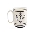A white ceramic mug with a handle, decorated with minimalist black line art of a face and small gold accents, set against a plain white background.