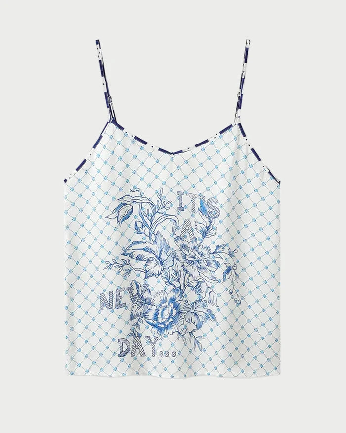 The ME369 Angelique Camisole is a white top with thin straps, showcasing a blue geometric check print and an intricate blue floral design on the front. Inspired by the original style, this camisole also features the phrase "IT'S A NEW DAY" printed in blue among the flowers.