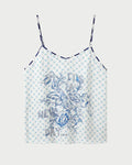 The ME369 Angelique Camisole is a white top with thin straps, showcasing a blue geometric check print and an intricate blue floral design on the front. Inspired by the original style, this camisole also features the phrase "IT'S A NEW DAY" printed in blue among the flowers.