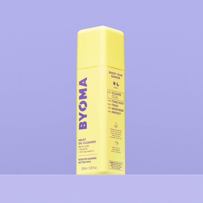 A yellow bottle of Byoma Milky Oil Cleanser, angled view showing the "Boost Your Barrier" routine steps on the side panel, on a purple background.