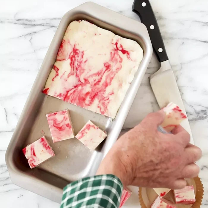 Top view of stainless steel mini jelly roll pan with marbled white and pink fudge squares and a knife on a marble countertop