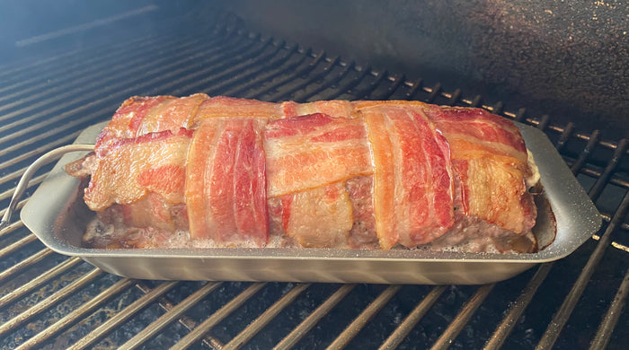 Side view of stainless steel mini jelly roll pan with rolled rim holding bacon-wrapped meatloaf on grill grates