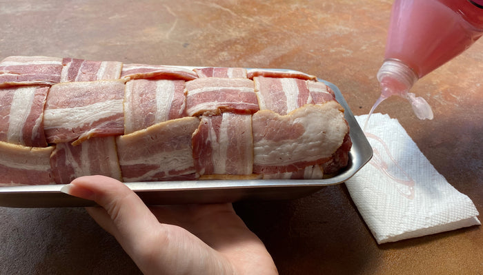 Angled view of Mini Jelly Roll Pan holding bacon-weave meatloaf, shallow stainless pan with rolled handles, held by hand