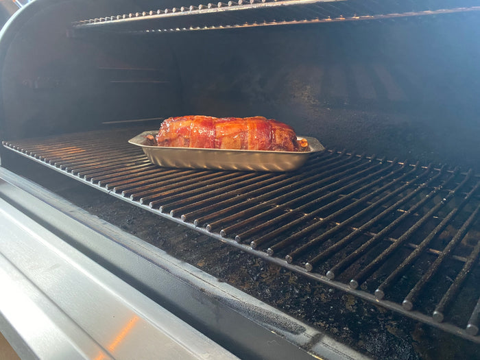 Angled view of Mini Jelly Roll Pan showcasing shallow stainless steel design holding a bacon-wrapped roast on a grill rack inside an open gas grill