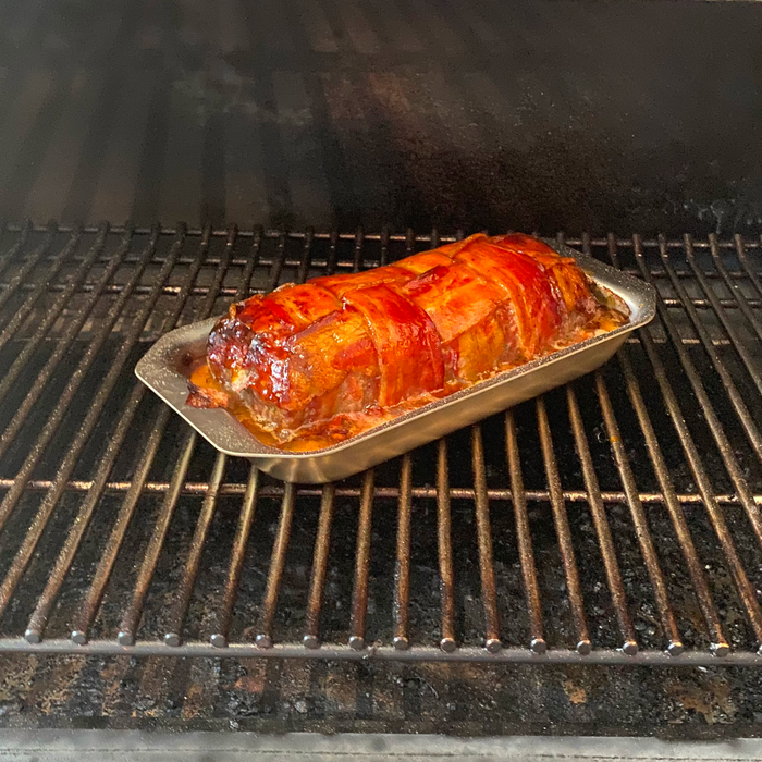 Angled view of stainless steel Mini Jelly Roll Pan showing shallow rolled handles holding a bacon-wrapped glazed meatloaf on an oven rack