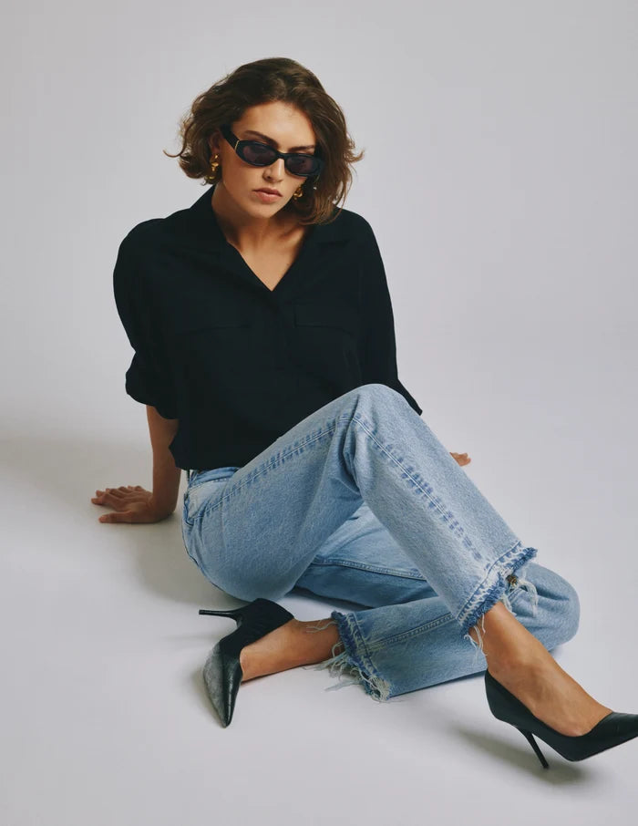 Woman wearing a black top and light blue jeans sitting on a white background