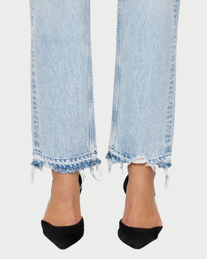 Light blue jeans with frayed hems worn by a person on a white background