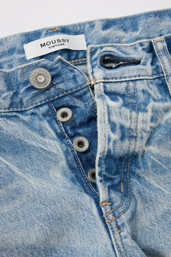 Close-up of Moussy Wildwood Straight Leg Jeans in light blue denim, featuring a partially open button fly with visible metal buttons, orange stitching, and a white "MOUSSY" label at the waistband; expertly made in Japan.