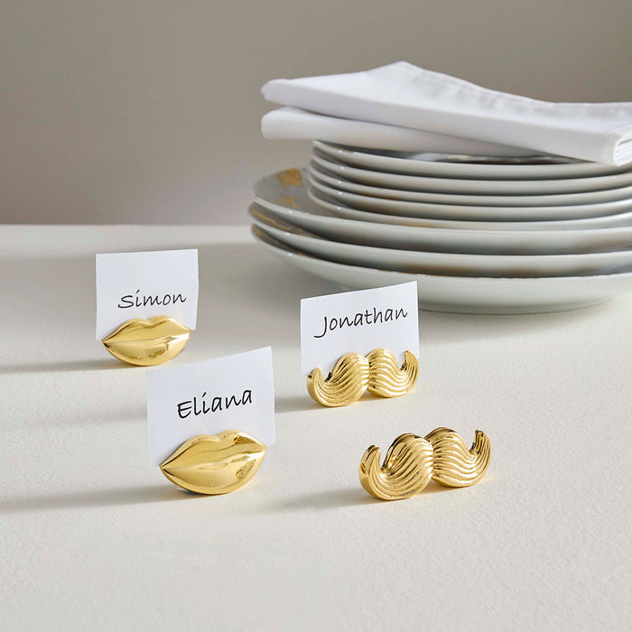 Gold mustache and lip-shaped place card holders with name cards on a neutral background
