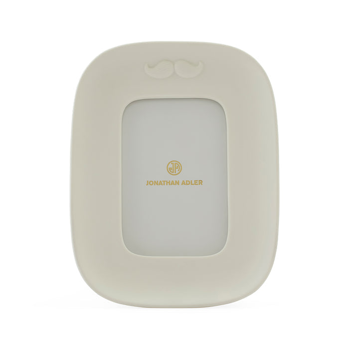 A cream-colored picture frame with a small mustache detail at the top and gold 'JONATHAN ADLER' branding in the center, shown on a plain white background.