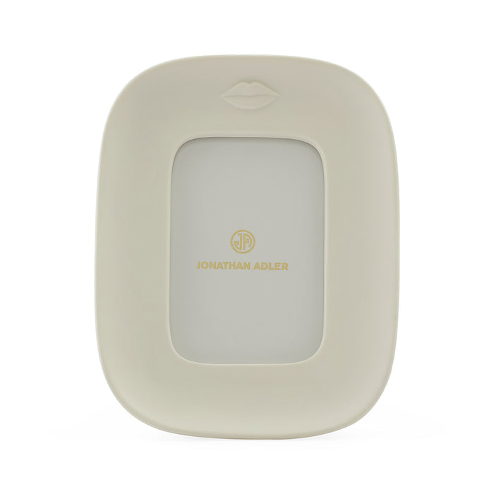 Jonathan Adler picture frame in a warm cream color with a gold logo and a subtle lips icon at the top, shown on a clean white background.