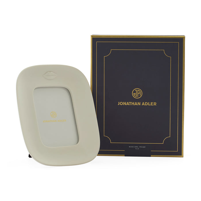 A cream-colored Jonathan Adler picture frame with a gold logo, shown next to its black and gold branded presentation box on a white background.
