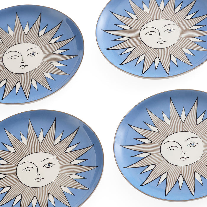 Four round ceramic plates arranged in a 2x2 grid on a white background. Each plate features a light blue border and a central white sun face design with gray rays outlined in black.