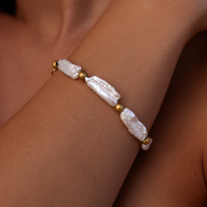 Unique open ocean pearl bracelet featuring long natural pearls and textured gold beads on a tan wrist