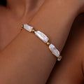 Unique open ocean pearl bracelet featuring long natural pearls and textured gold beads on a tan wrist
