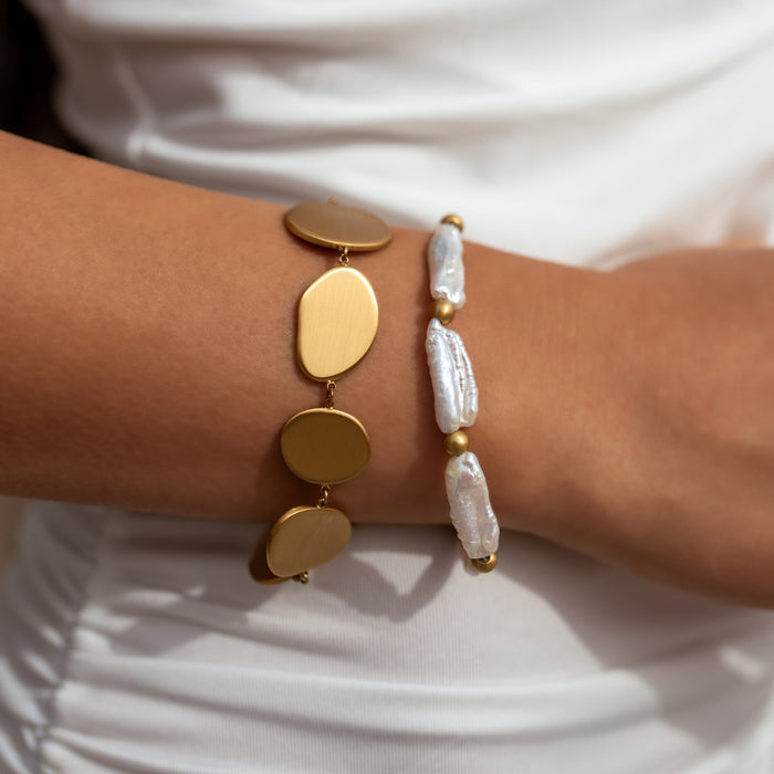 Gold and pearl bracelet on a wrist against a white background