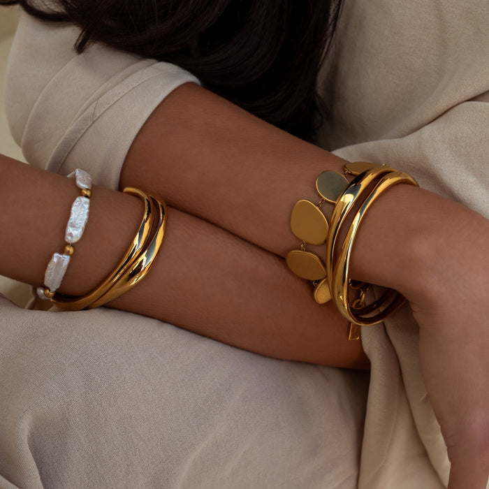 bracelet stacks with organic shaped gold cuffs, natural pearls and organic discs on tan wrists in a neutral outfit