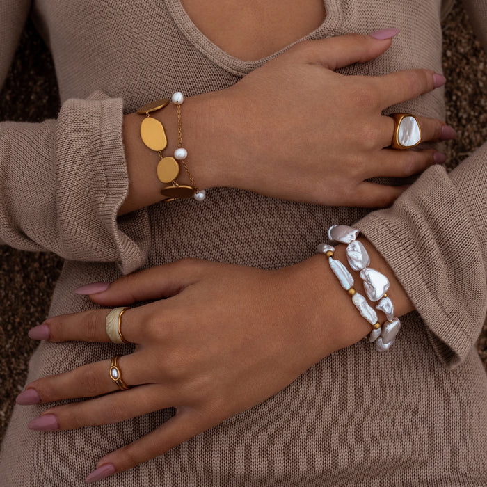 Close-up of hands wearing gold and pearl  jewelry on a neutral background