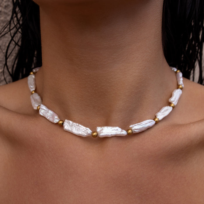 Open ocean pearl necklace with gold textured bead accents and long unique pearls on a person's neck