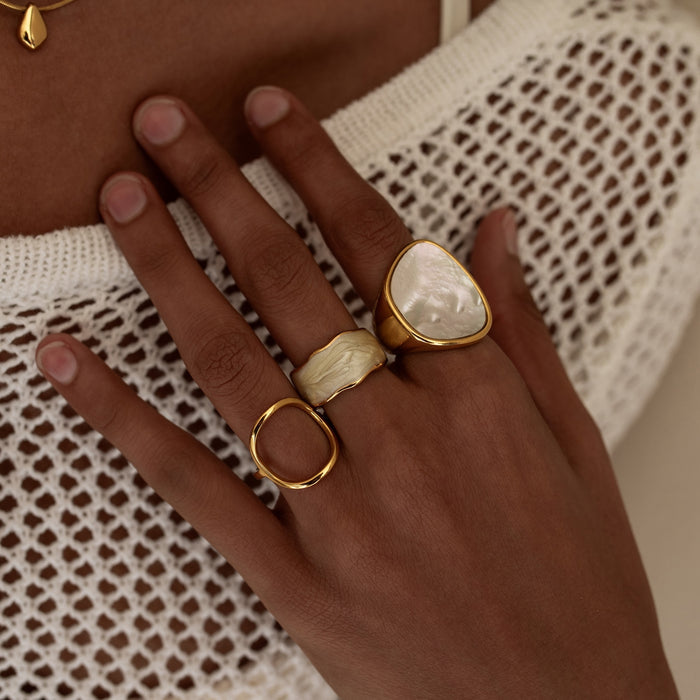 Hand wearing two gold rings with a textured white garment background