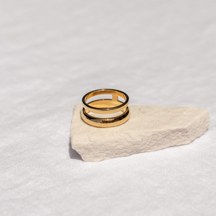 Double layer smooth gold ring sitting on a stone with a neutral background