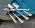 Close-up of Old Harbor flatware showing engraved decorative handles on spoons and forks on a ceramic plate with teal napkin