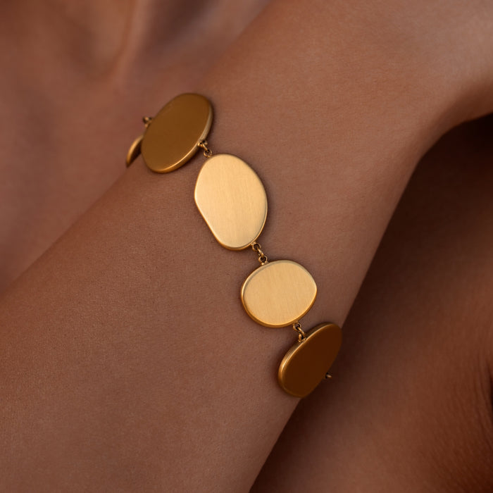 Gold disc bracelet with round flat organic shaped pendants on a wrist against a tan background