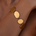 Gold disc bracelet with round flat organic shaped pendants on a wrist against a tan background