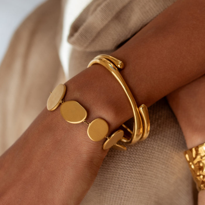 Gold bracelet with circular links on a wrist against a neutral background