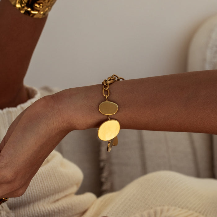 Gold circle disc bracelet on a wrist with a neutral background