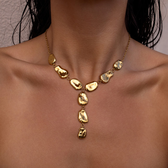 Gold Y necklace with organic shaped oval pendants on a woman against a neutral background