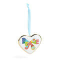 A heart-shaped white ornament with a gold-toned border, featuring the word 'PEACE' in colorful retro letters and a peace sign, hanging from a light blue ribbon on a white background.