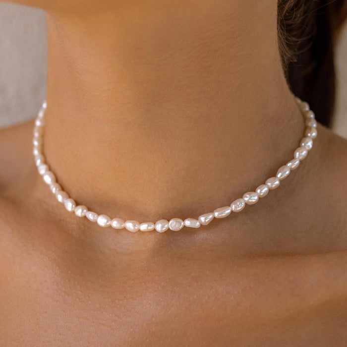 Small pearl necklace worn by a person on a neutral background