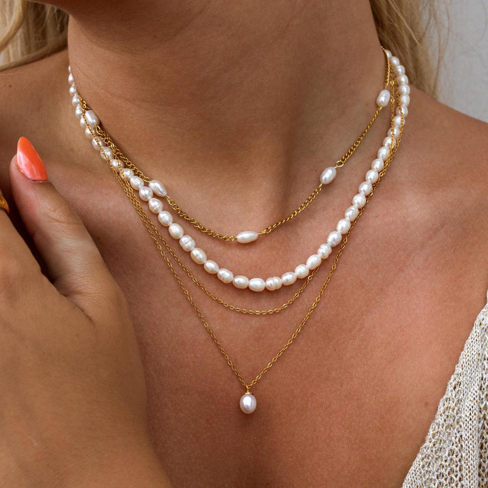 Gold and pearl necklace stack on a person featuring dainty gold chains and small freshwater pearls