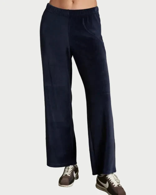 Person wearing navy blue pants and sneakers on a plain background