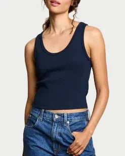 Woman wearing a navy tank top and blue jeans against a beige background
