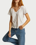 A person with long red hair wears the Perfectwhitetee Hendrix Basic V-Neck T-Shirt in white by perfectwhitetee and blue jeans, posing with one hand in their pocket before a light-colored fabric backdrop.