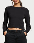 A woman in the perfectwhitetee Jamie Recycled LS Tee Black by perfectwhitetee, a boxy fit crewneck, pairs it with high-waisted black jeans. She stands against a light background with her hands in her pockets, face partially out of frame.