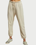 A person wears Perfectwhitetee Johnny Sweatpant - Sugar joggers in light beige French terry cotton with an elastic drawstring waist and cuffs, paired with white and metallic sneakers, standing against a plain background.